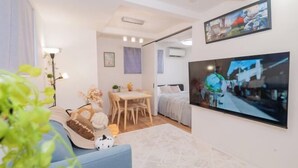 A modern living room with a sofa, a dining table, and a TV mounted on the wall. - New Garfieldhome Shinjuku (Tokyo)