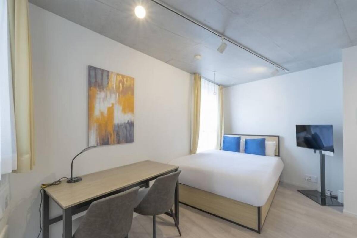 Una camera d'albergo con un letto, una scrivania, una sedia, una televisione e opere d'arte alle pareti.