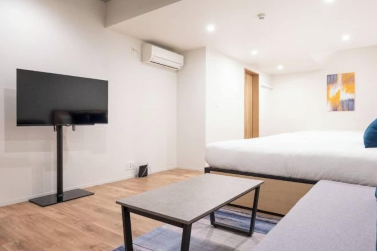 A modern hotel room with a bed, a flat-screen TV, a small table, and an air conditioning unit.