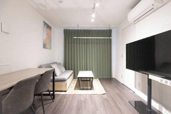 A modern living room with a sofa, a dining table, chairs, a coffee table, a flat-screen TV, and a large window with curtains. - LEGALAND Hatagaya ANNEX (Tokyo)
