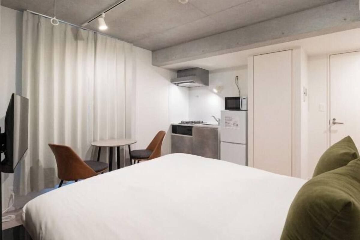 Una camera d'albergo con un letto, una scrivania, una sedia, una televisione e angolo cottura.