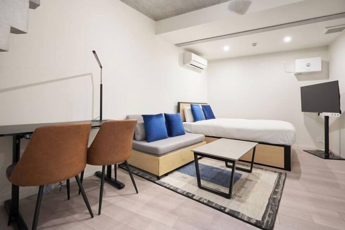 A modern bedroom with a bed, a desk, two chairs, and a TV.