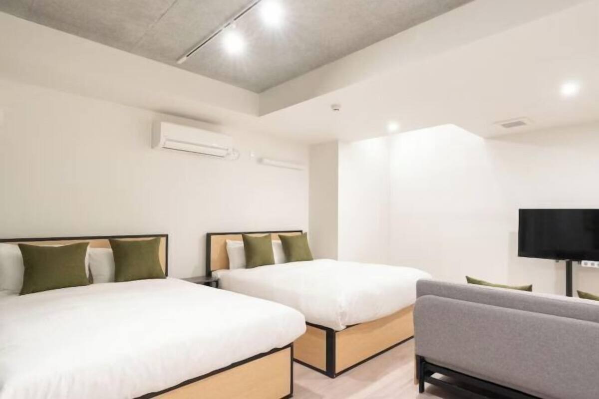 Una camera d'albergo con due letti, un divano, una televisione a schermo piatto e un condizionatore d'aria.