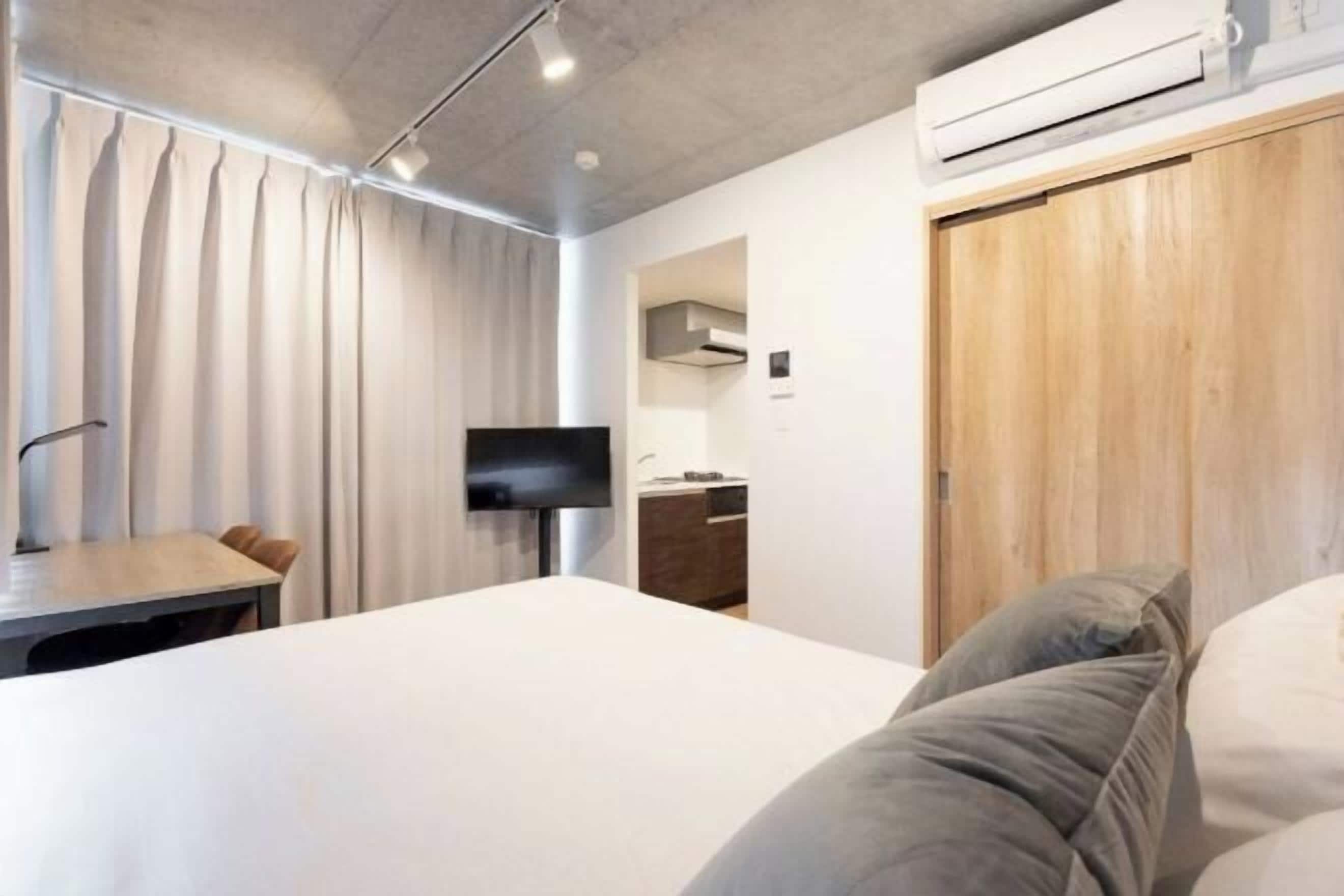 A modern hotel room with a bed, a desk, a TV, and a wooden wardrobe.