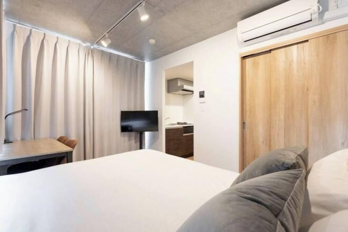 A modern hotel room with a bed, a desk, a TV, and a wooden wardrobe.