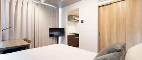 A modern hotel room with a bed, a desk, a TV, and a wooden wardrobe.