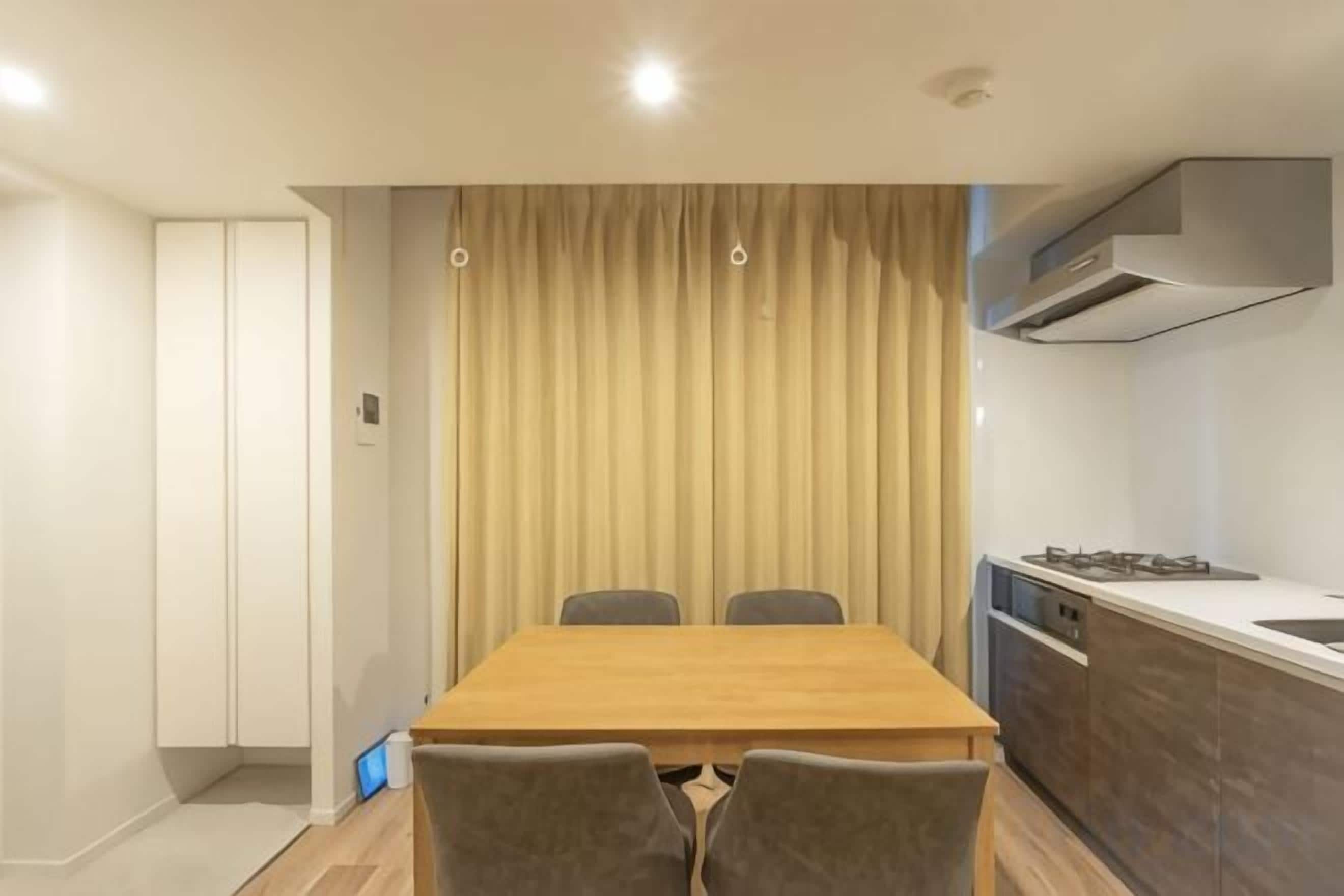 A modern kitchen with a dining area, including a wooden table and chairs, a built-in stove, and a large window with curtains.