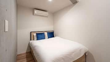 A bedroom with a bed, wooden flooring, a white wall, and a ceiling light.