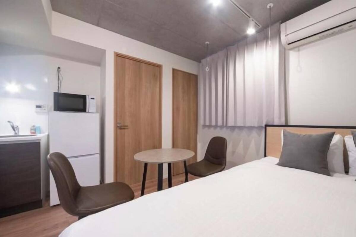 Una camera d'albergo con un letto, un tavolino, due sedie, un forno a microonde e un armadio.