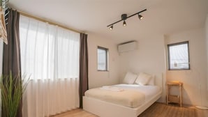 Een slaapkamer met een bed, gordijnen, een potplant en een kleine tafel.