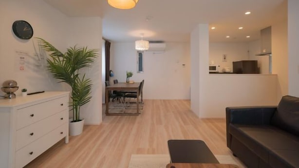 Een moderne woonkamer met een bank, een eethoek met tafel en stoelen, een potplant en een plafondlamp.