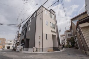 Un edificio residenziale a più piani con facciata piatta, ingresso visibile e vista sulla strada con un veicolo parcheggiato.