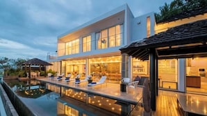 Une maison moderne dotée d’une piscine, d’un espace salon extérieur et d’une grande salle à manger avec de grandes fenêtres.