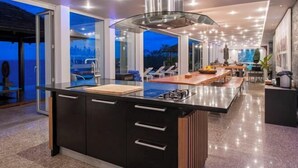 Une cuisine moderne dotée d’un îlot central, de grandes fenêtres et offrant une vue sur l’extérieur.