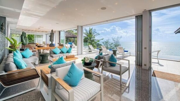 Une chambre d’hôtel moderne dotée d’un grand balcon, de sièges confortables et offrant une vue sur l’océan.