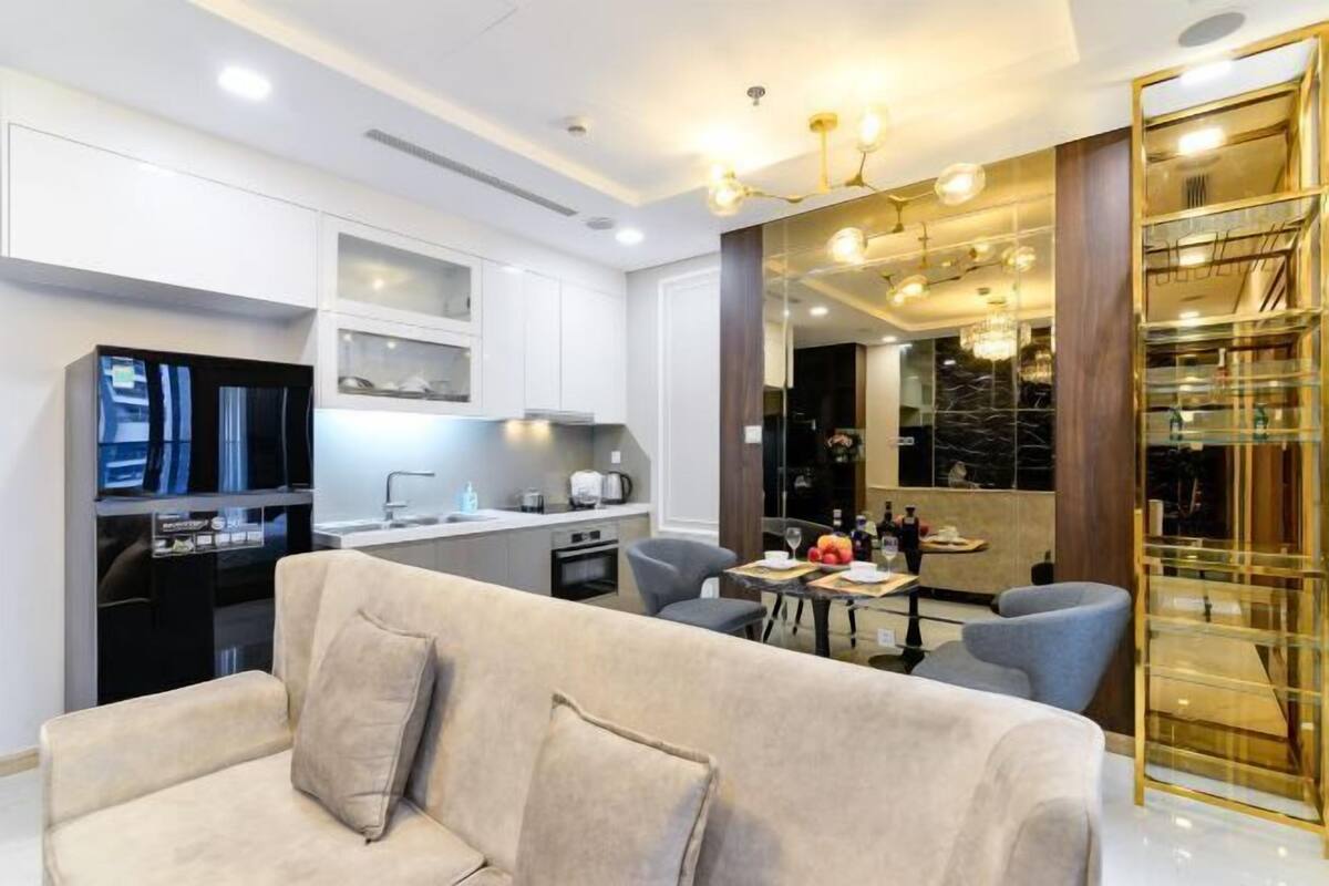 A modern living room with a sofa, a dining table with chairs, a kitchen area, and a glass display cabinet.