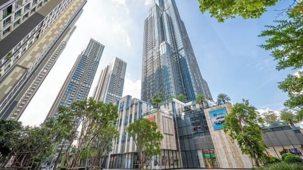 Un moderno edificio de gran altura con fachada de vidrio, rodeado de palmeras y otra vegetación.