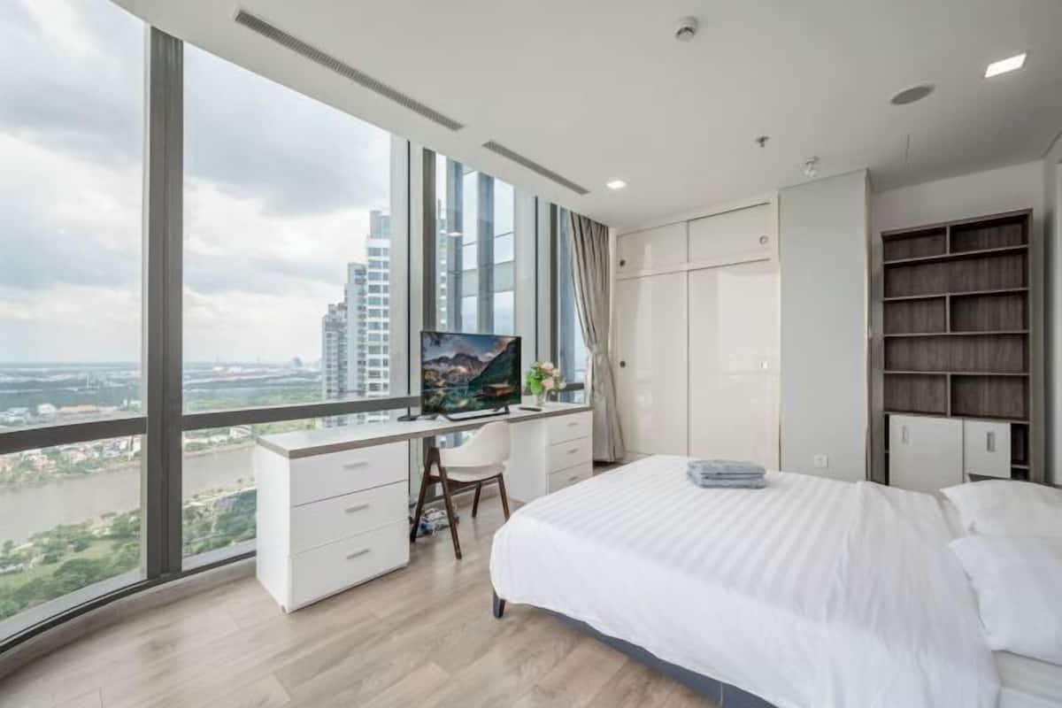 A modern bedroom with a large bed, a desk with a computer, and a view of the city.