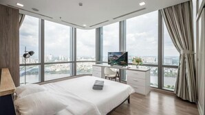 Habitación de hotel moderna con una cama grande, un escritorio con televisión y vistas a la ciudad a través de amplias ventanas.