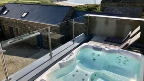 A hot tub on a balcony with a view of the sea and a stone building. - Tan y Garn - 2 Bedroom Cottage - Whitesands (Saint David's and the Cathedral Close)