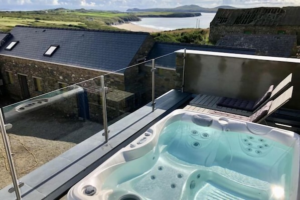 A hot tub on a balcony with a view of the sea and a stone building. - Tan y Garn - 2 Bedroom Cottage - Whitesands (Saint David's and the Cathedral Close)