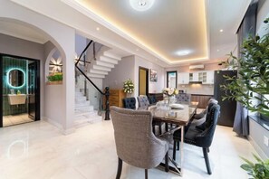 Un espace repas moderne avec une table en verre, deux chaises rembourrées, un escalier et une cuisine en arrière-plan.