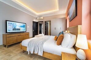 Une chambre d’hôtel moderne équipée d’un lit, d’une télévision, d’une commode en bois et d’une porte donnant accès à une salle de bain.