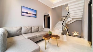 A modern living room with a sectional sofa, a staircase with a railing, and a framed picture on the wall. - KN3 Holiday Villa (Ho Chi Minh City)