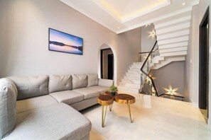 Ein modernes Wohnzimmer mit einem Ecksofa, einer Treppe mit Geländer und einem gerahmten Bild an der Wand.