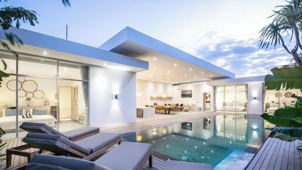 Ein moderner Poolbereich mit Liegestühlen, einem gläsernen Wohnraum und freiem Blick auf den Pool.