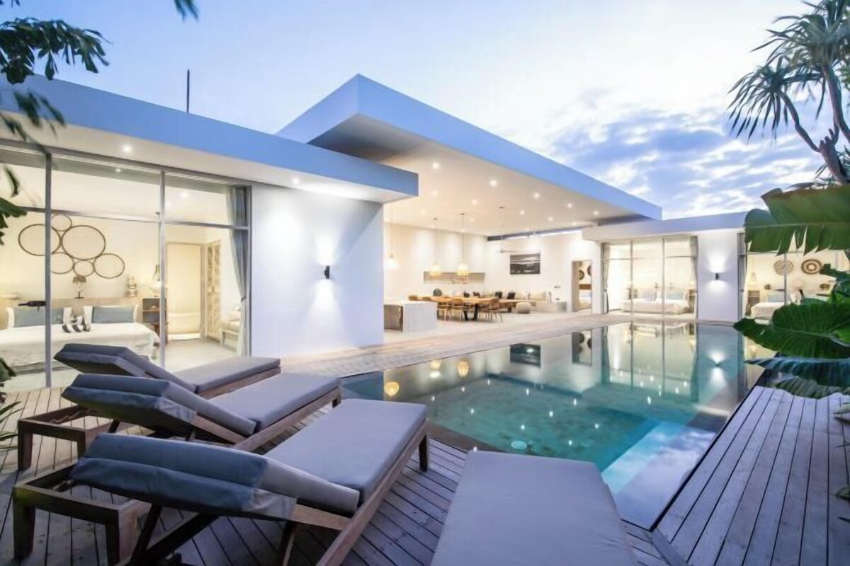 A modern poolside area with lounge chairs, a glass-enclosed living space, and a clear view of the pool.