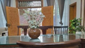 A dining table with a glass top and a vase of white flowers. - RU YI HOTEL(SMC-PRIVATE) LIMITED (Islamabad)