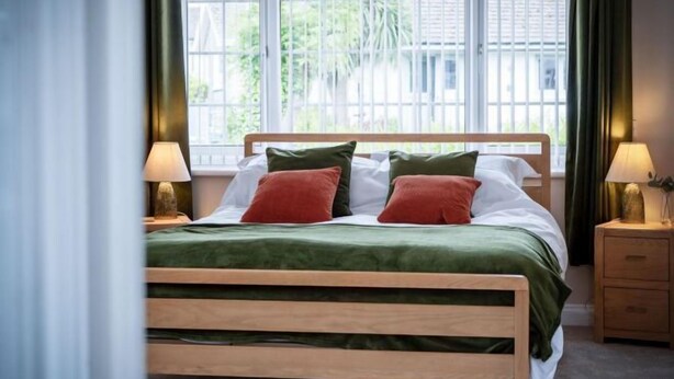 A bed with a wooden frame, green bedding, and two pillows. There are two bedside tables with lamps.