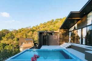Una casa moderna con piscina, ventanas amplias y vista a una ladera boscosa.