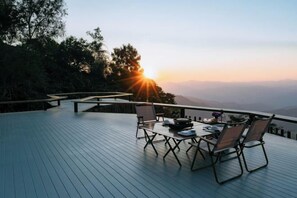 An outdoor deck with a table and chairs, overlooking a mountainous landscape. - Misty Valley Doichang (Mae Suai)