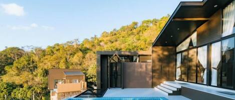 Una casa moderna con piscina, ventanas amplias y vistas a una ladera boscosa.