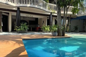 A pool area with a wooden deck, a lounge area with seating, and a covered outdoor space with plants. - Zinnia (Maafushi)