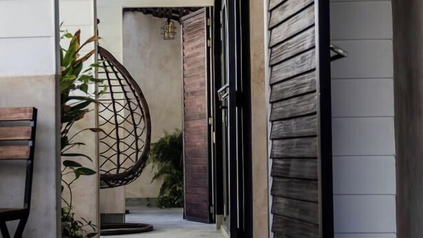 A narrow hallway with a wooden door, a hanging chair, and a bench. - Zinnia (Maafushi)