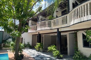 A two-story building with a balcony, potted plants, and a pool area.