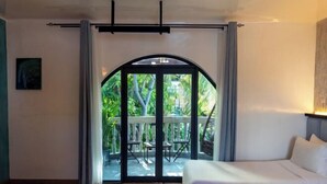 A bedroom with a large bed, a sliding glass door leading to an outdoor area with a wooden deck and chairs. - Zinnia (Maafushi)