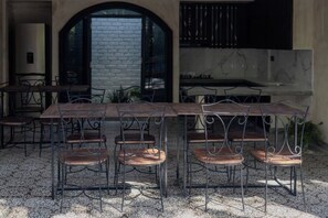 A dining area with a long table and chairs, a brick wall, and a window.