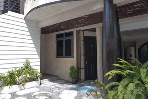 A modern building with a curved facade, a large central pillar, and a small garden area with potted plants. - Zinnia (Maafushi)