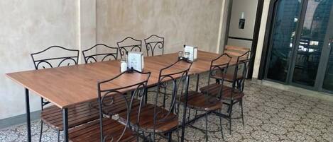 A dining area with a long wooden table and chairs, a refrigerator, and a tiled floor.