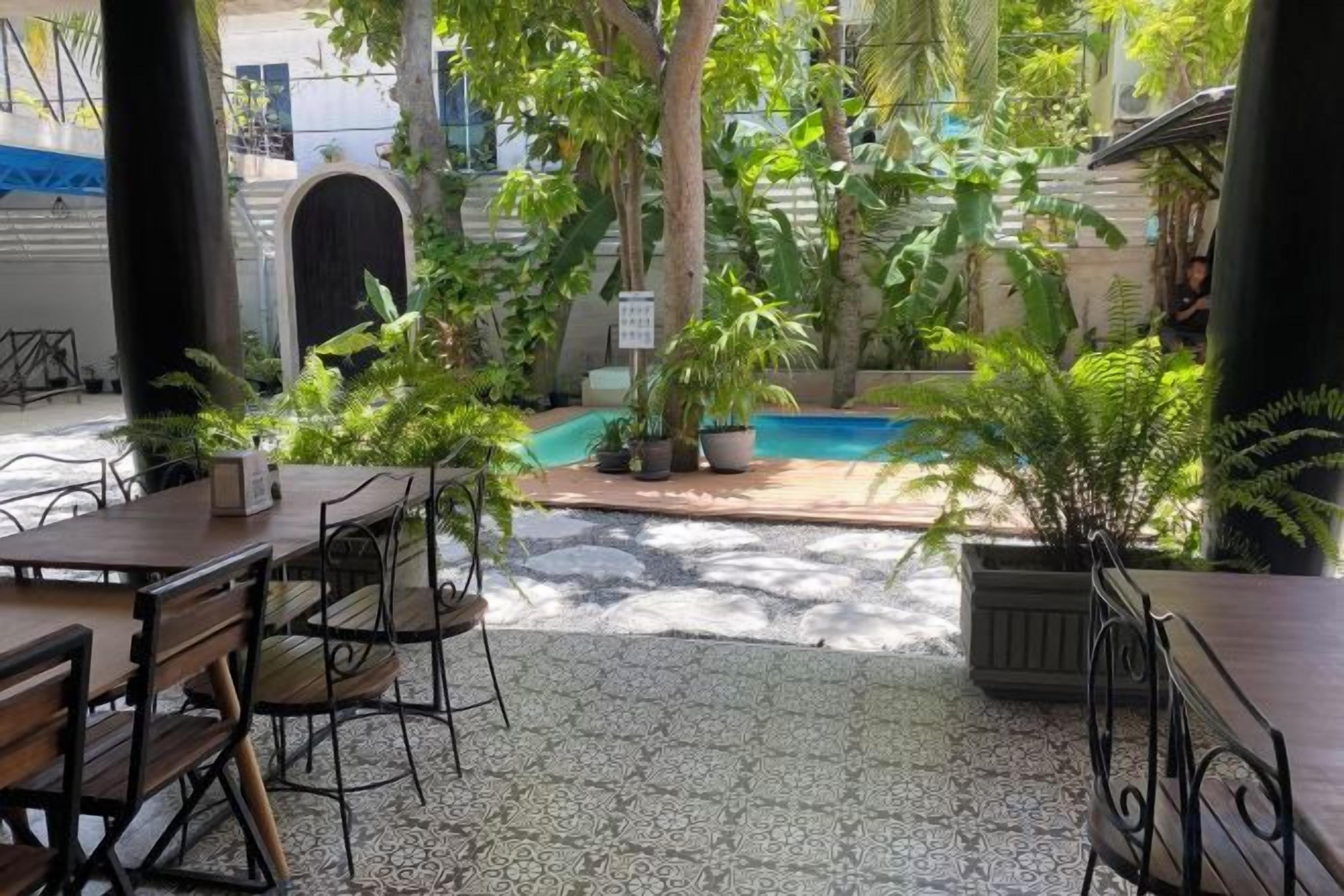 Un espacio al aire libre con mesas y sillas, rodeado de plantas en macetas y una piscina.