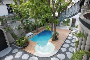 A swimming pool with a wooden deck, surrounded by plants and a stone pathway. - Zinnia (Maafushi)