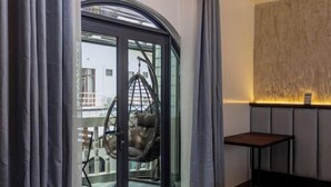 A room with a glass door leading to an outdoor area, a hanging chair, a small table, and a textured wall. - Zinnia (Maafushi)