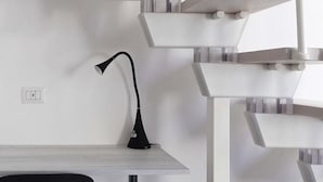 Ein modernes Zimmer mit Schreibtisch, einer schwarzen Schreibtischlampe und einer weißen Wendeltreppe.