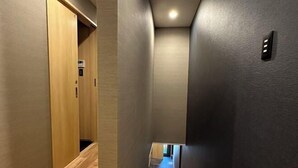 A narrow hallway with wooden flooring, a door on the left, and a light switch on the right wall. - Kin・ Tengachaya8-14 (Osaka)