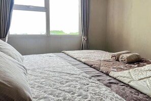 Una cama bien hecha con ropa de cama estampada, una ventana con cortinas y vistas al exterior a zonas verdes.