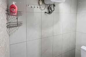 Un baño con pared de azulejos, un lavamanos, un grifo y un cabezal de ducha.